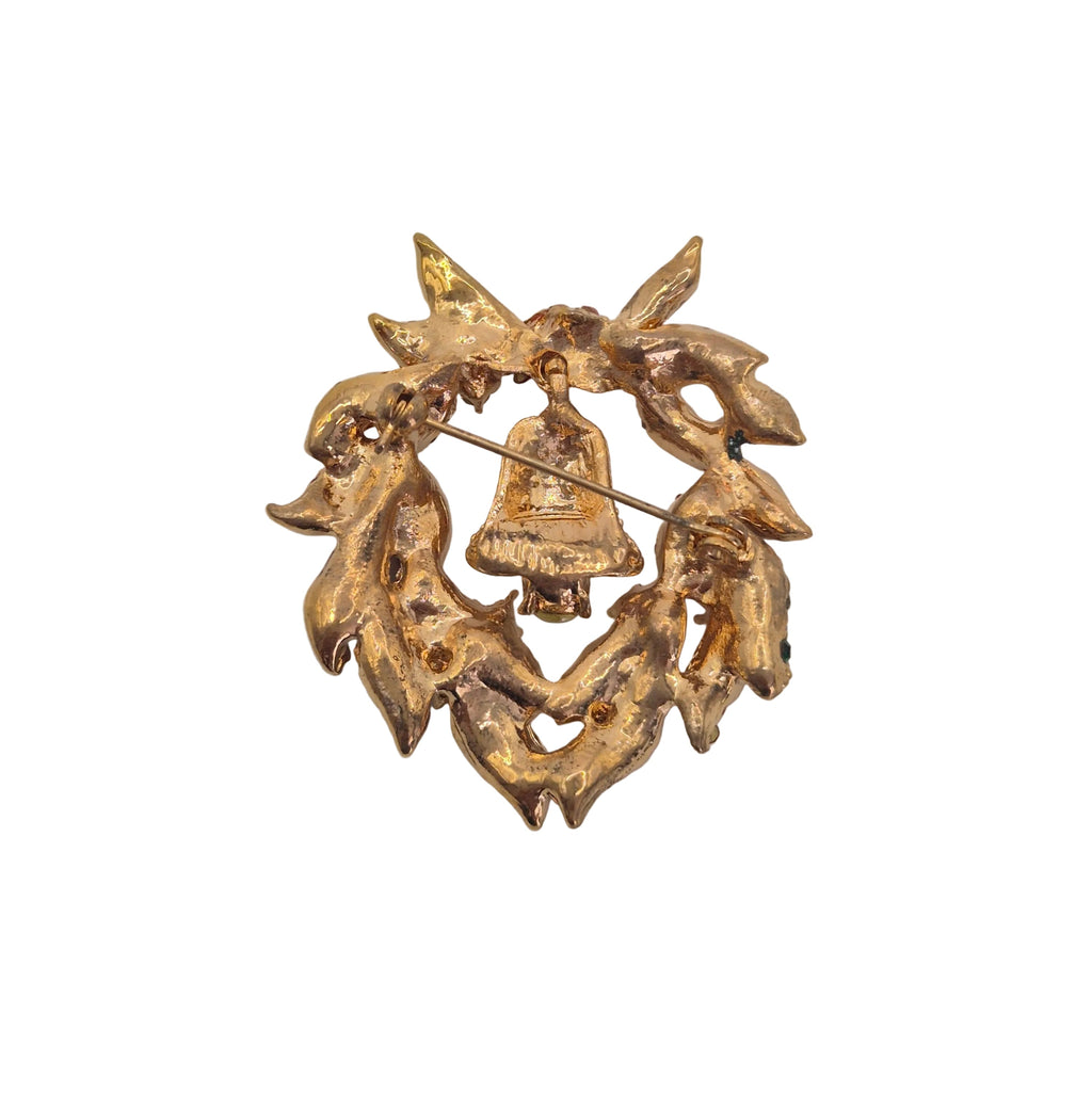 A gold-toned Christmas wreath brooch featuring a small hanging bell in the center, photographed on a plain white background.