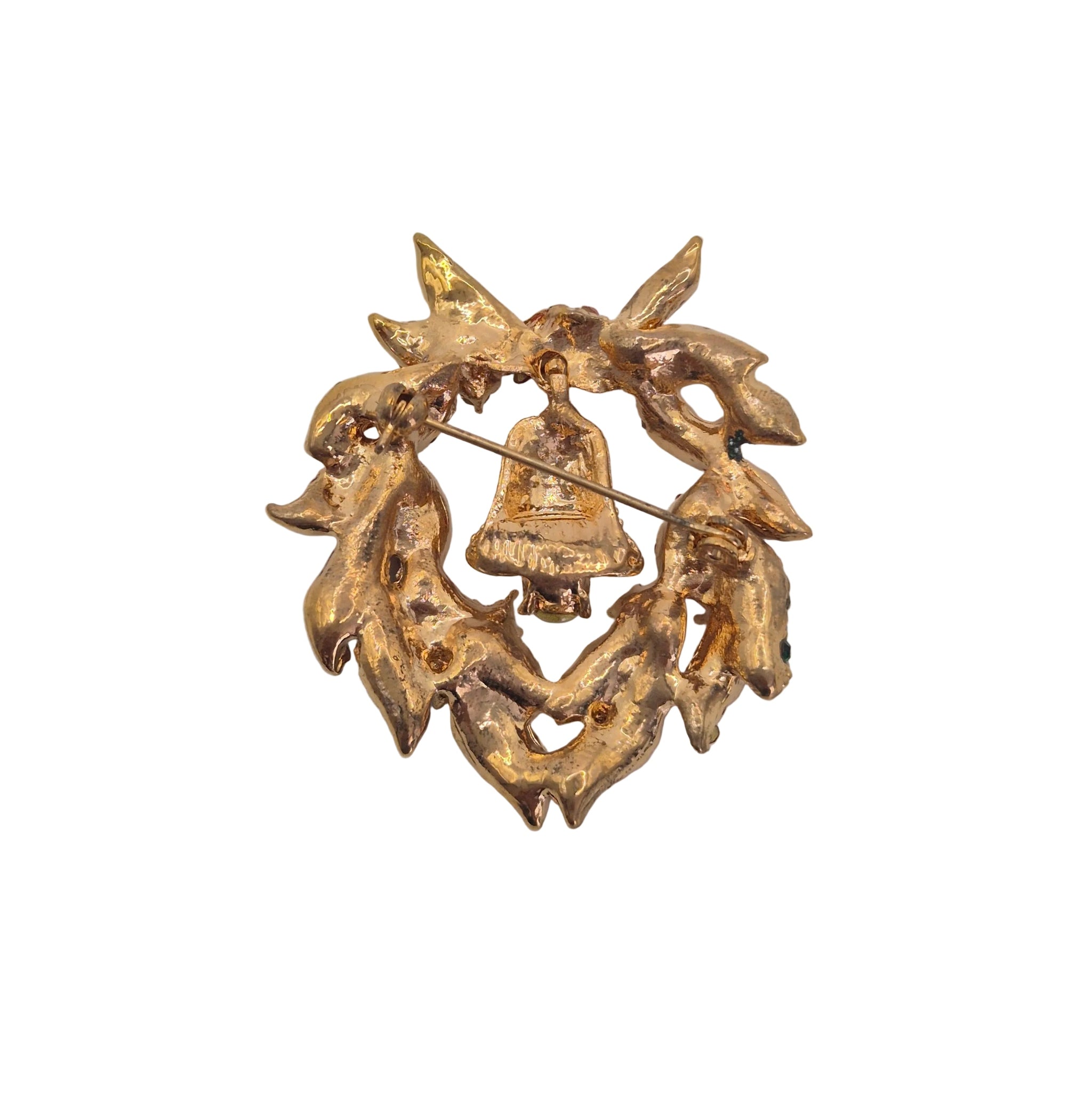 A gold-toned Christmas wreath brooch featuring a small hanging bell in the center, photographed on a plain white background.
