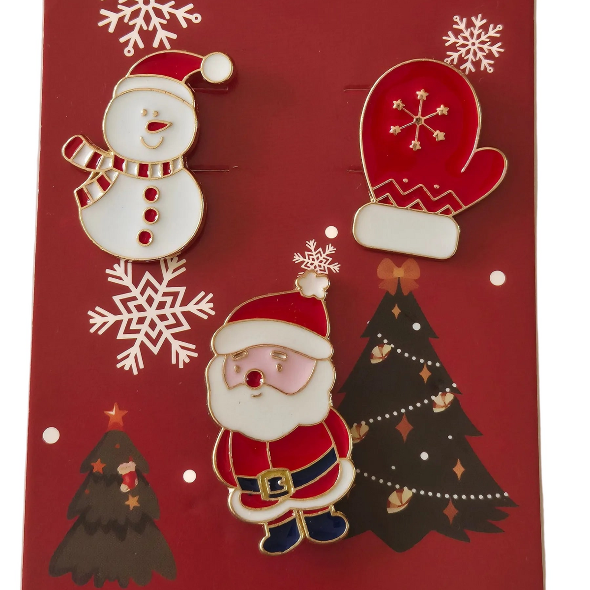 Three Christmas-themed enamel pins attached to a red backing card: a white snowman, a red mitten with gold snowflake detail, and a Santa Claus figure. The backing card features gold and white snowflakes and Christmas tree illustrations.