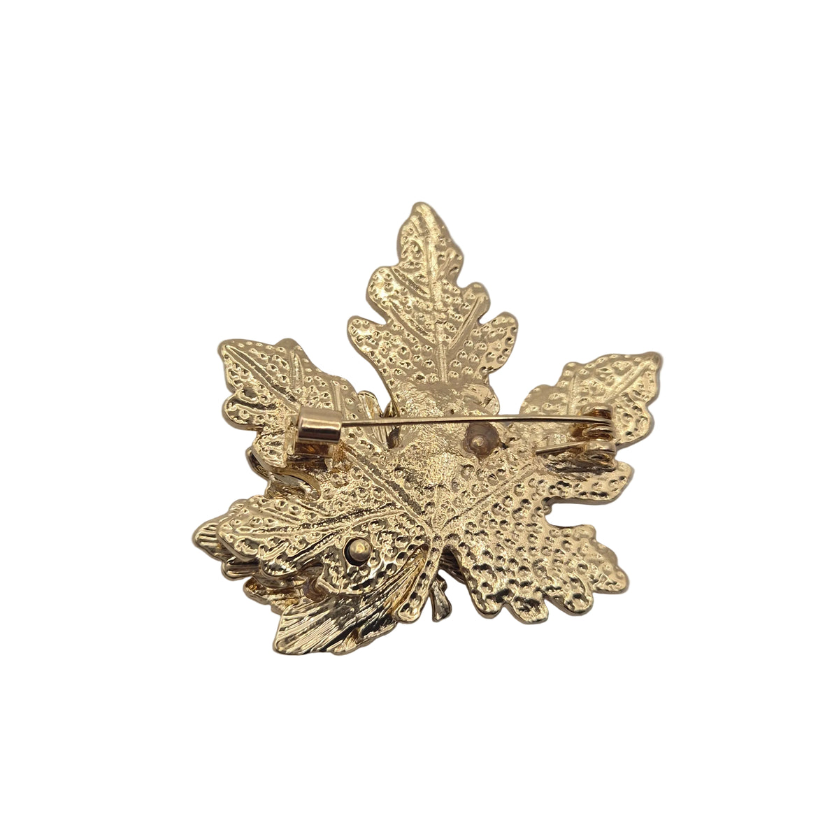 A gold-colored metal leaf-shaped brooch with a textured finish and a pin clasp visible on the reverse side, photographed on a plain white background.