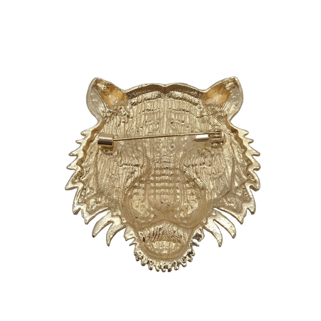 A gold-colored tiger head brooch with a textured, engraved surface and a pin clasp on the underside, shown against a plain white background.