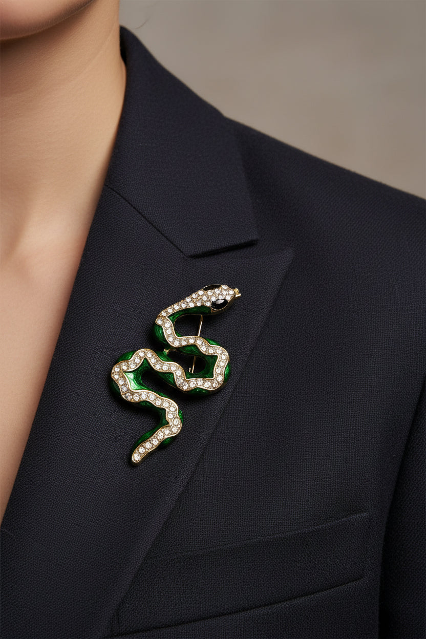 A gold-plated snake-shaped brooch with dark green enamel and clear rhinestones, being worn on a blazer.