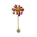 A gold-toned firework brooch with deep red enamel petals, small clear rhinestones, and a dangling chain ending in a snowflake-shaped gold-toned charm, shown on a plain white background.