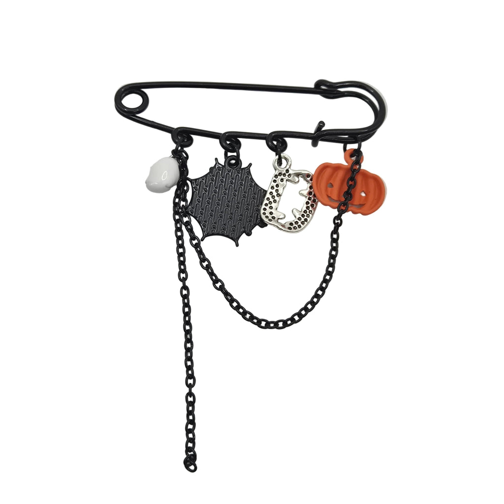 A black safety pin brooch with dangling charms, including a black spider web, a silver spider, a white pom-pom, and an orange jack-o'-lantern, on a light gray background.