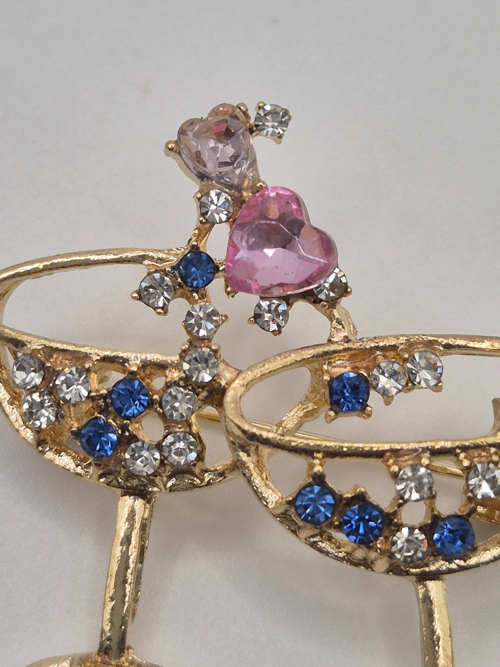 Gold brooch with pink, blue, and clear gemstones on a light gray background