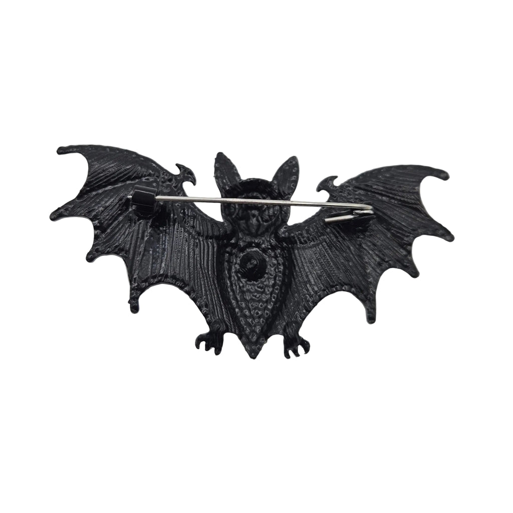 A black bat-shaped brooch with spread wings and a silver safety pin back, shown on a plain white background.