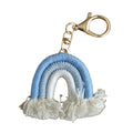 A small rainbow-shaped keychain charm with blue and white braided yarn and white fringe, attached to a gold-tone lobster clasp, on a plain white background.
