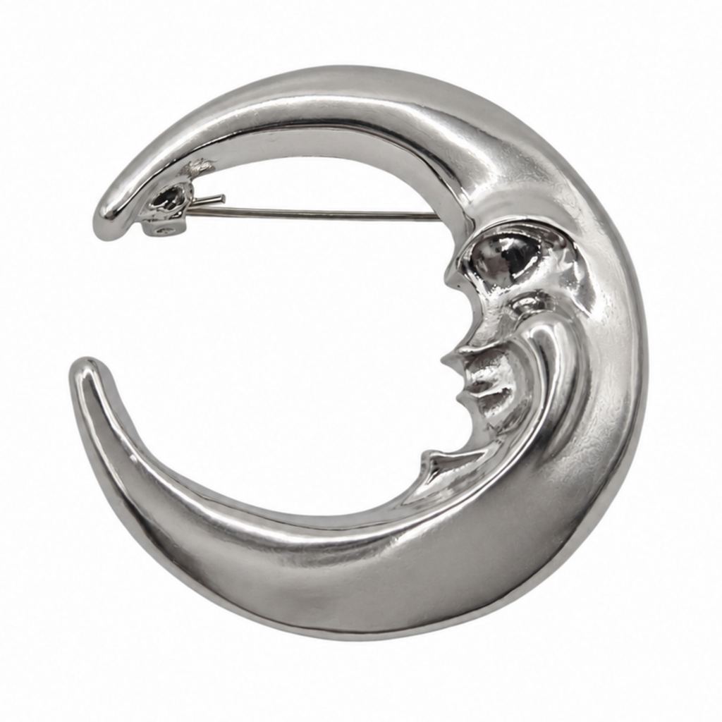A polished silver crescent moon brooch with a stylized face, shown on a plain white background.