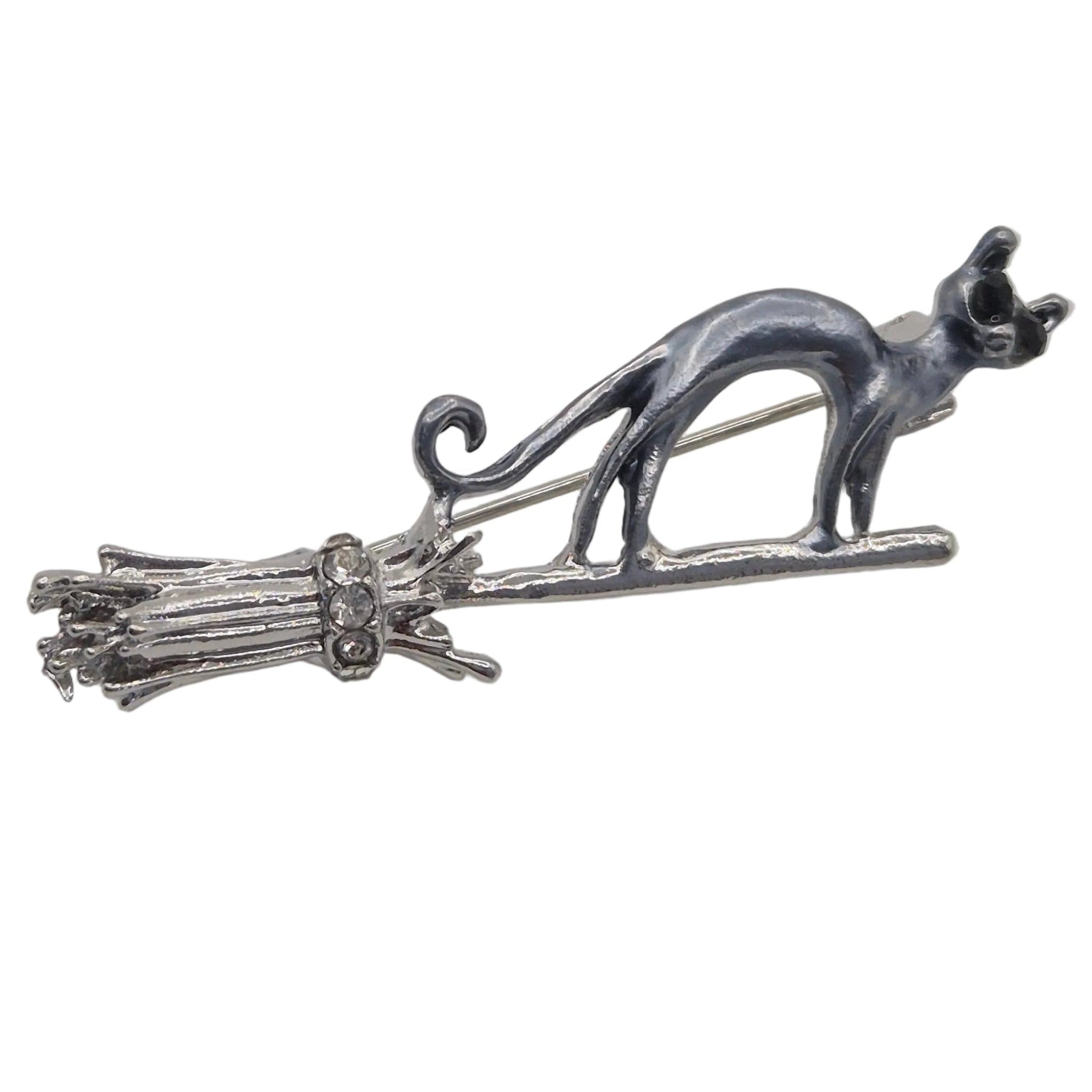 A silver and grey toned metal brooch featuring a cat standing on a broomstick, photographed against a plain white background.