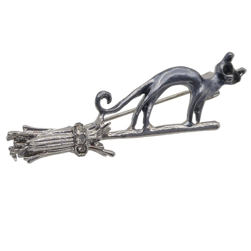 A silver and grey toned metal brooch featuring a cat standing on a broomstick, photographed against a plain white background.