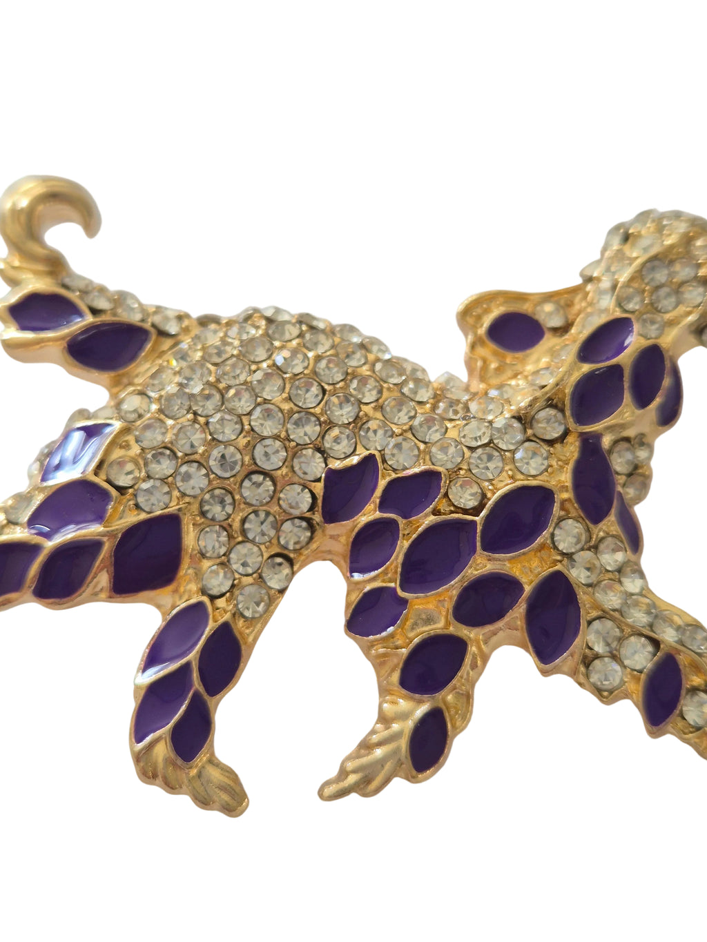 Decorative brooch with gold, purple, and clear gemstones on a white background