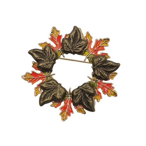 A vintage-style circular brooch featuring dark metallic leaf shapes with red and gold maple leaf accents, displayed on a plain white background.
