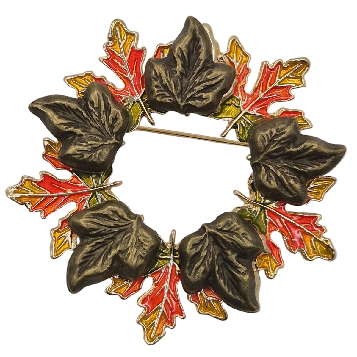 An autumn-themed metal brooch featuring a circular wreath design composed of dark bronze ivy leaves and red, orange, and yellow maple leaves, set against a plain white background.