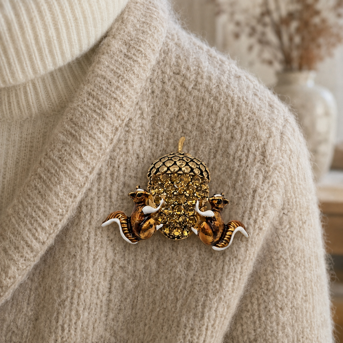 Two bronze-tone squirrels holding a large sparkling acorn brooch, styled on a soft cream knitted jumper.