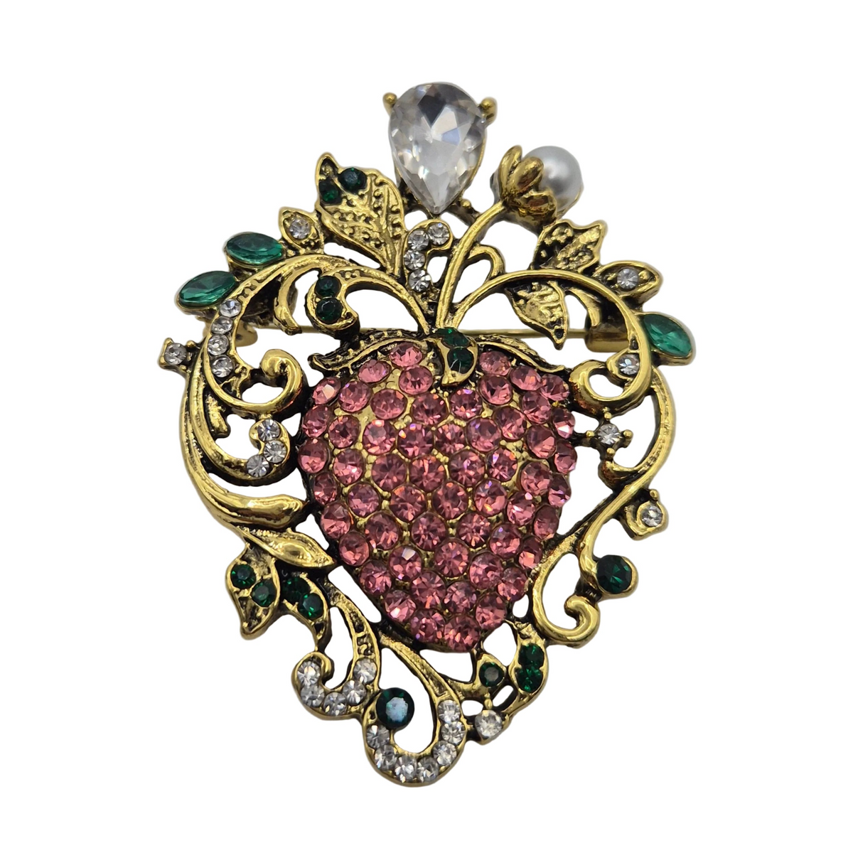 A vintage-style brooch shaped like a heart-shaped strawberry, featuring a pink rhinestone centre, gold-tone filigree scroll work, green emerald accents, a clear teardrop crystal, and a white pearl at the top, shown on a plain white background.