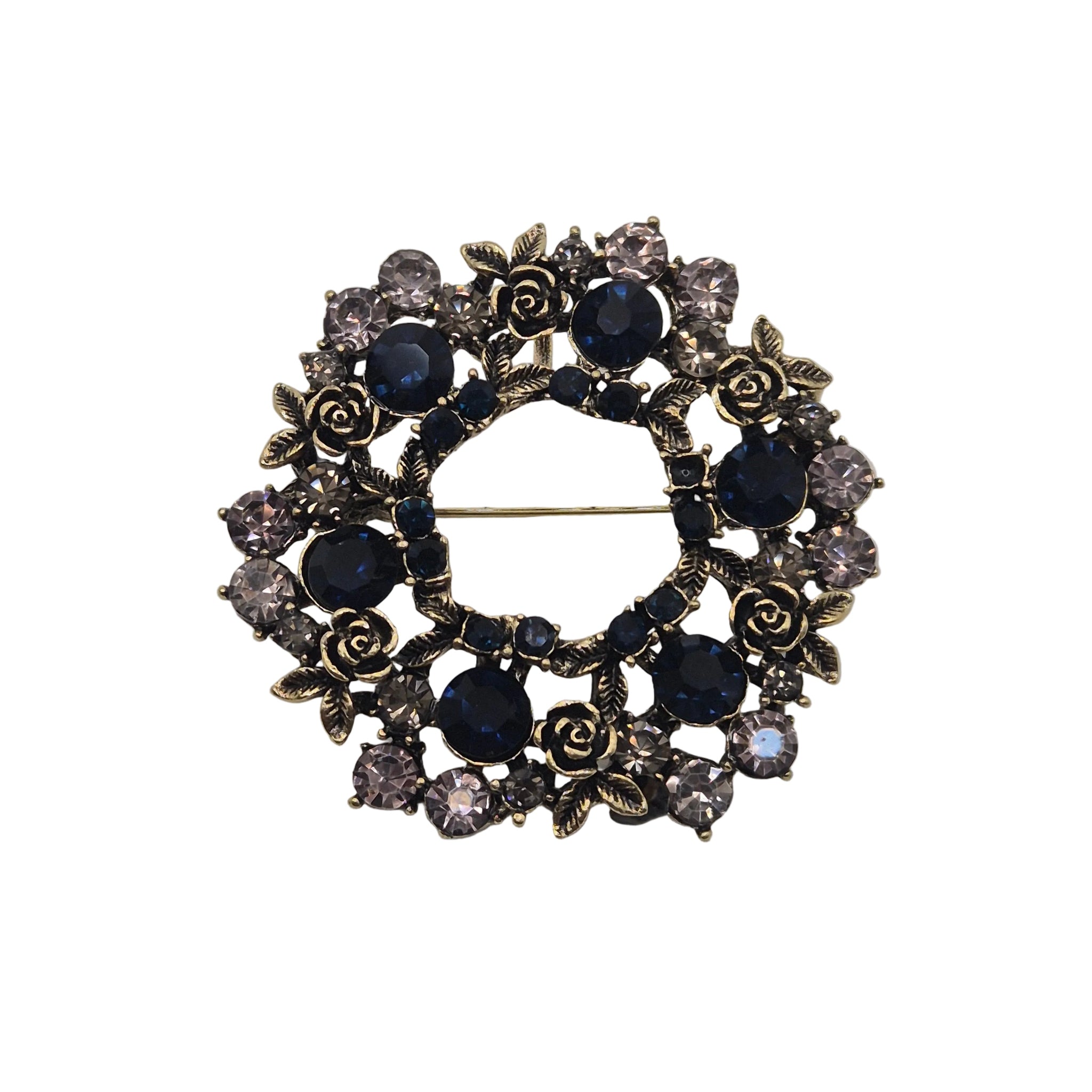 A vintage-style brooch featuring a circular design with dark blue faceted gemstones, antiqued gold-toned rose motifs, and clear rhinestones, photographed on a plain light gray background.