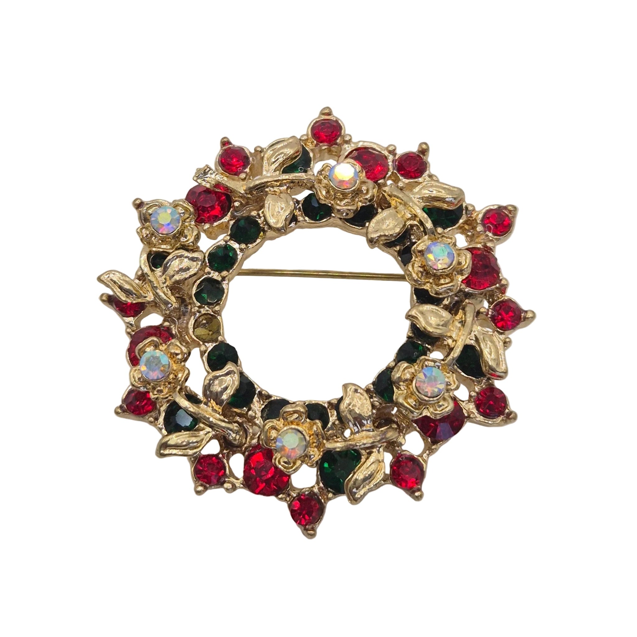 A gold-tone floral wreath brooch embellished with red, dark green, and clear rhinestones, displayed on a neutral light gray background.