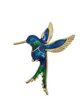 A hummingbird brooch featuring vibrant blue and green enamel with gold-tone metal outlines and wings, set against a plain white background.