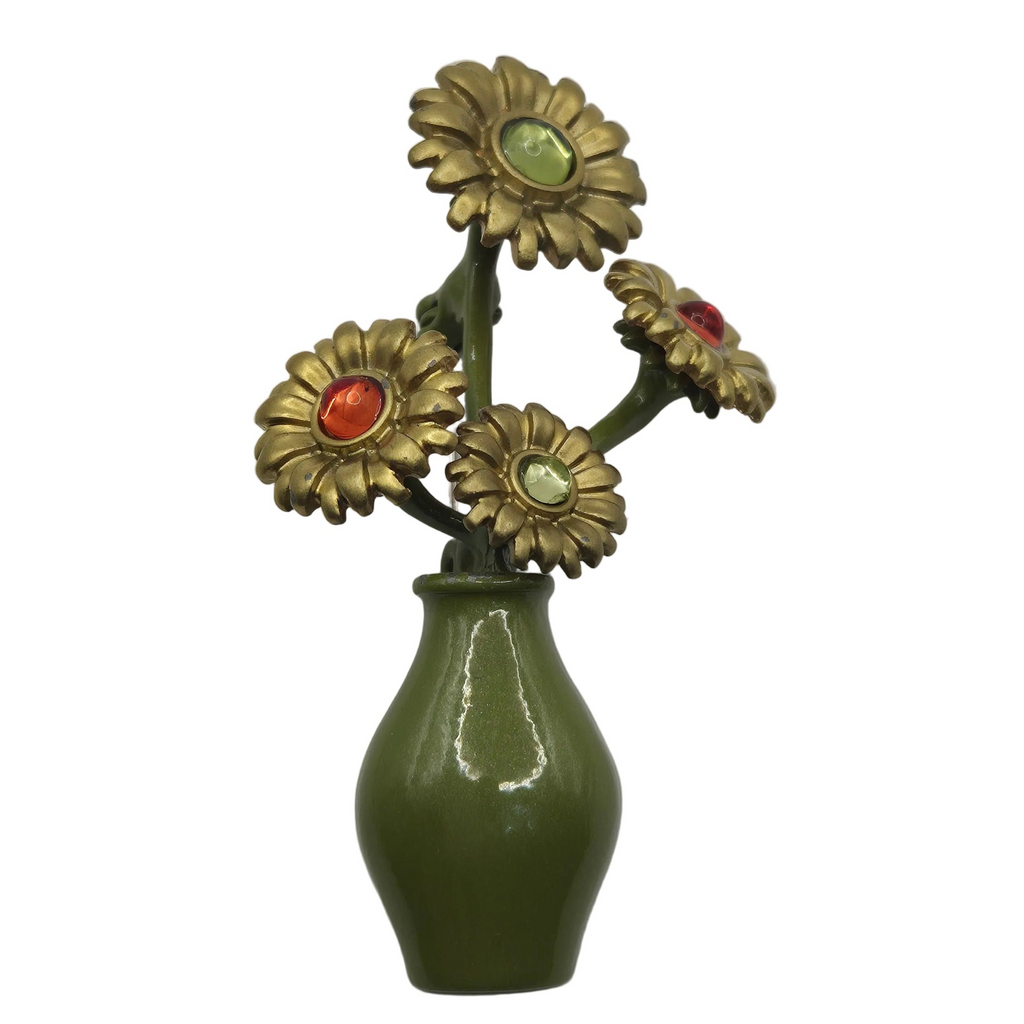 A vintage-style brooch with four bronze-toned flower heads set with colored stones (red, green, light green) on a glossy olive green ceramic vase, isolated on a white background.