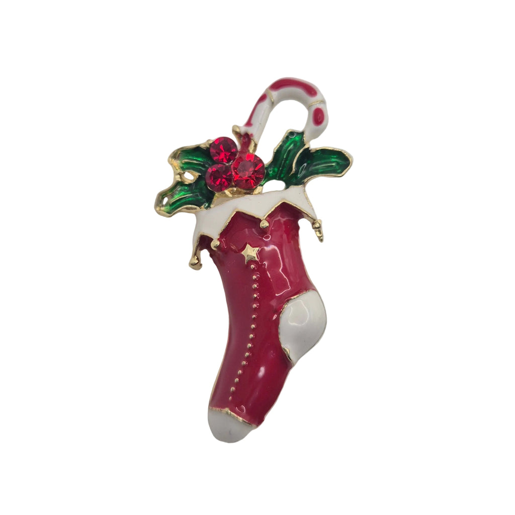 A Christmas stocking brooch featuring a glossy magenta-red body, white cuff and toe, green holly leaves, red berries, and a candy cane hanger, shown on a plain white background.