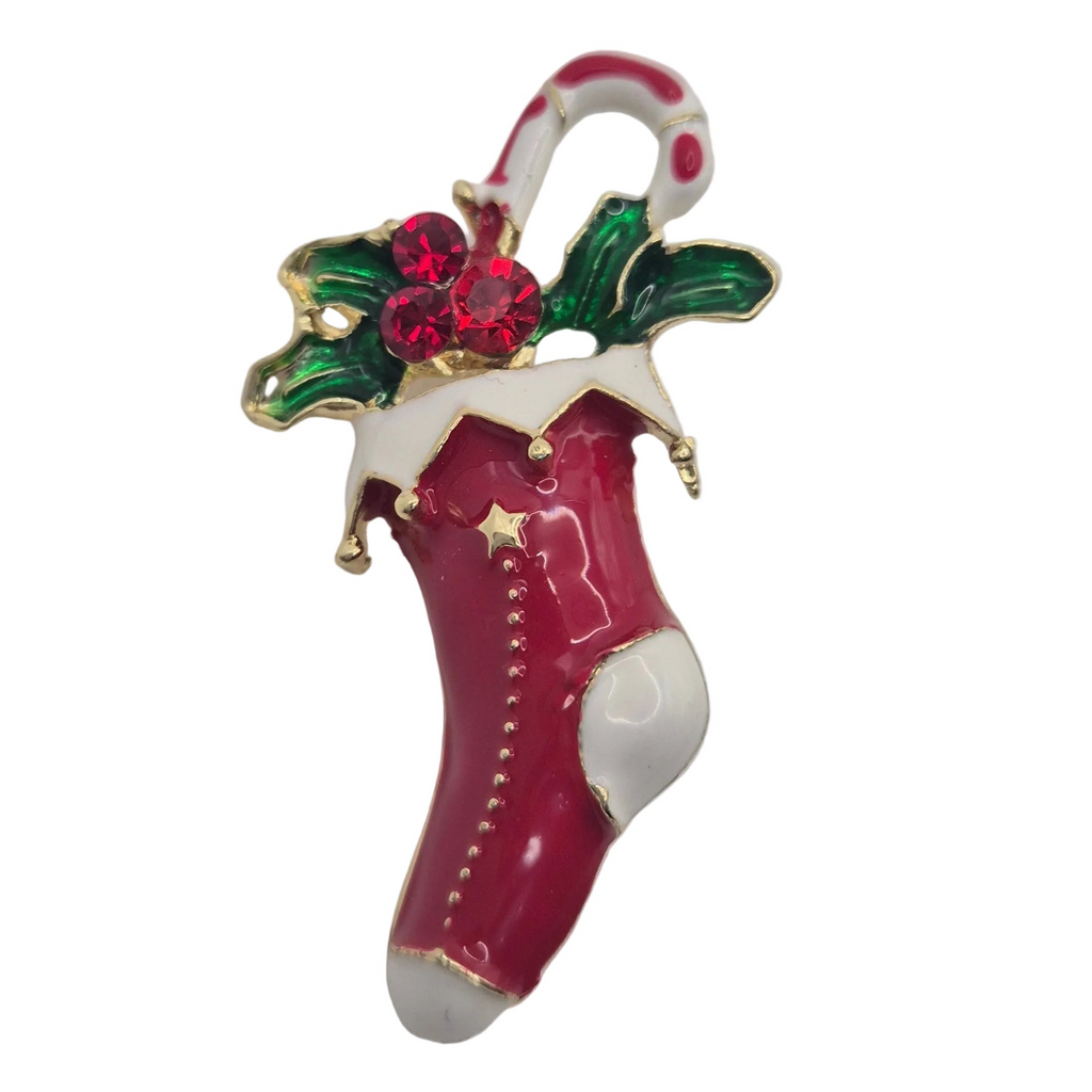 A Christmas stocking brooch featuring a glossy red and white stocking with gold trim, green holly leaves, and red crystal-like berries, attached to a white and red candy cane.
