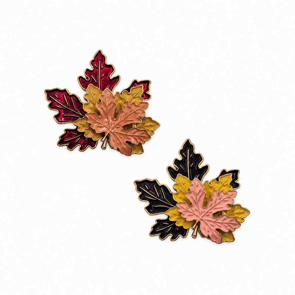 Two autumn maple leaf enamel pins on a white background, featuring pink, yellow, red, black, and gold colors.
