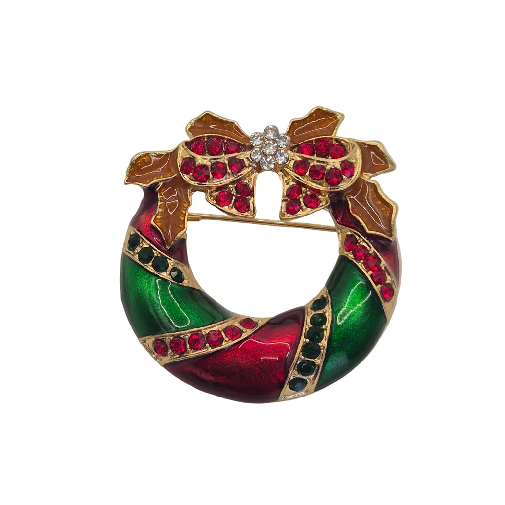 A gold tone Christmas wreath brooch featuring vibrant green and red enamel, accented with red rhinestones, brown holly leaves, and a central cluster of clear rhinestones.