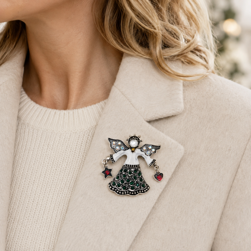 A close-up of a woman wearing a decorative angel brooch pinned to the lapel of her beige coat. The brooch features a white bod, black wings, and a black patterned skirt, with small red heart charms.