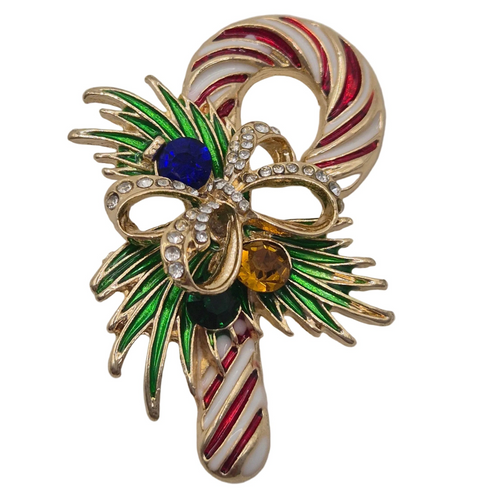 A festive Christmas candy cane brooch featuring gold-tone metal, red and white enamel stripes, green leaf accents, and three colorful rhinestone-encrusted gems in blue, amber, and dark green, set against a plain white background.