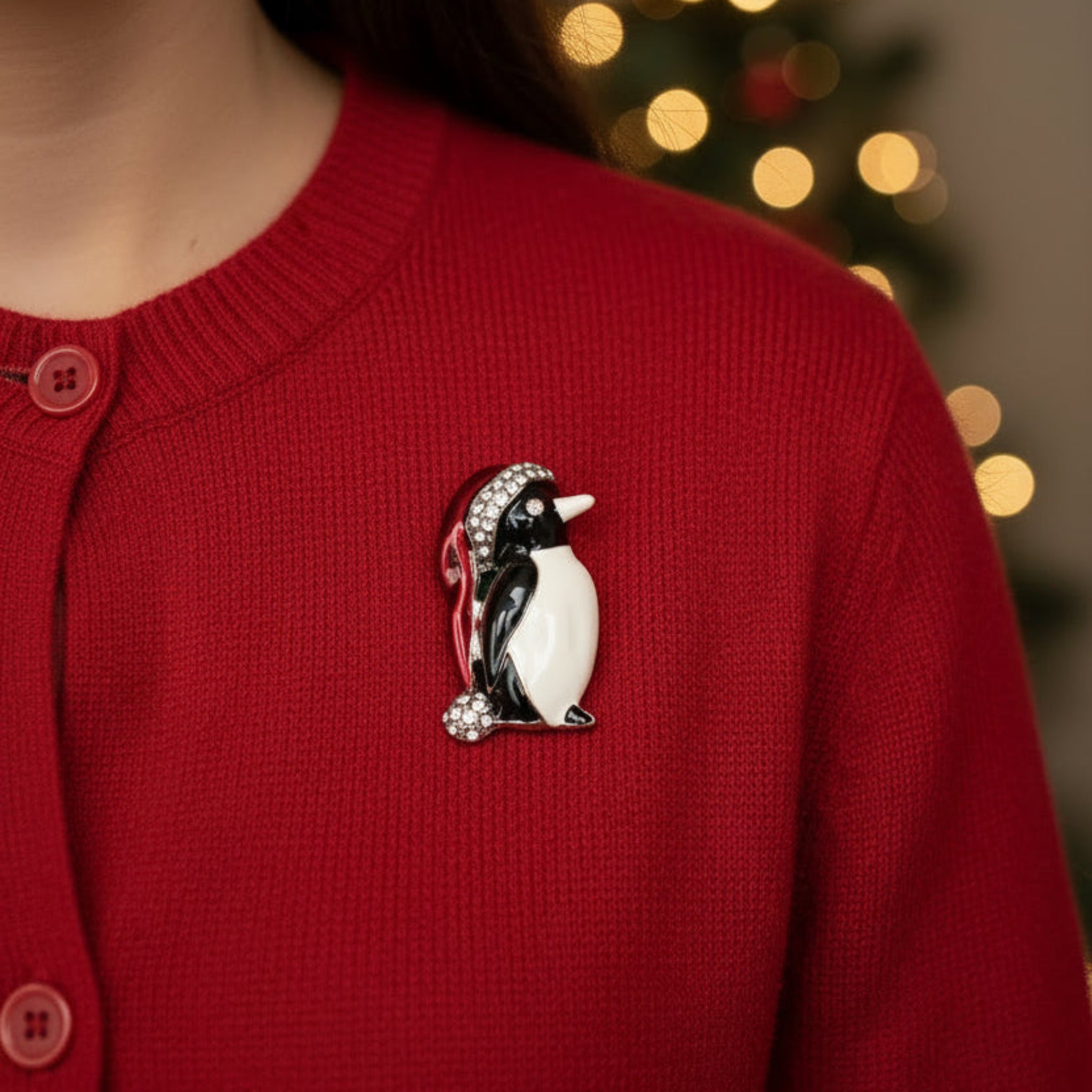 A penguin-shaped brooch featuring black and white enamel, a red Santa hat with rhinestone trim, and a small rhinestone ball, shown on a plain white background.
