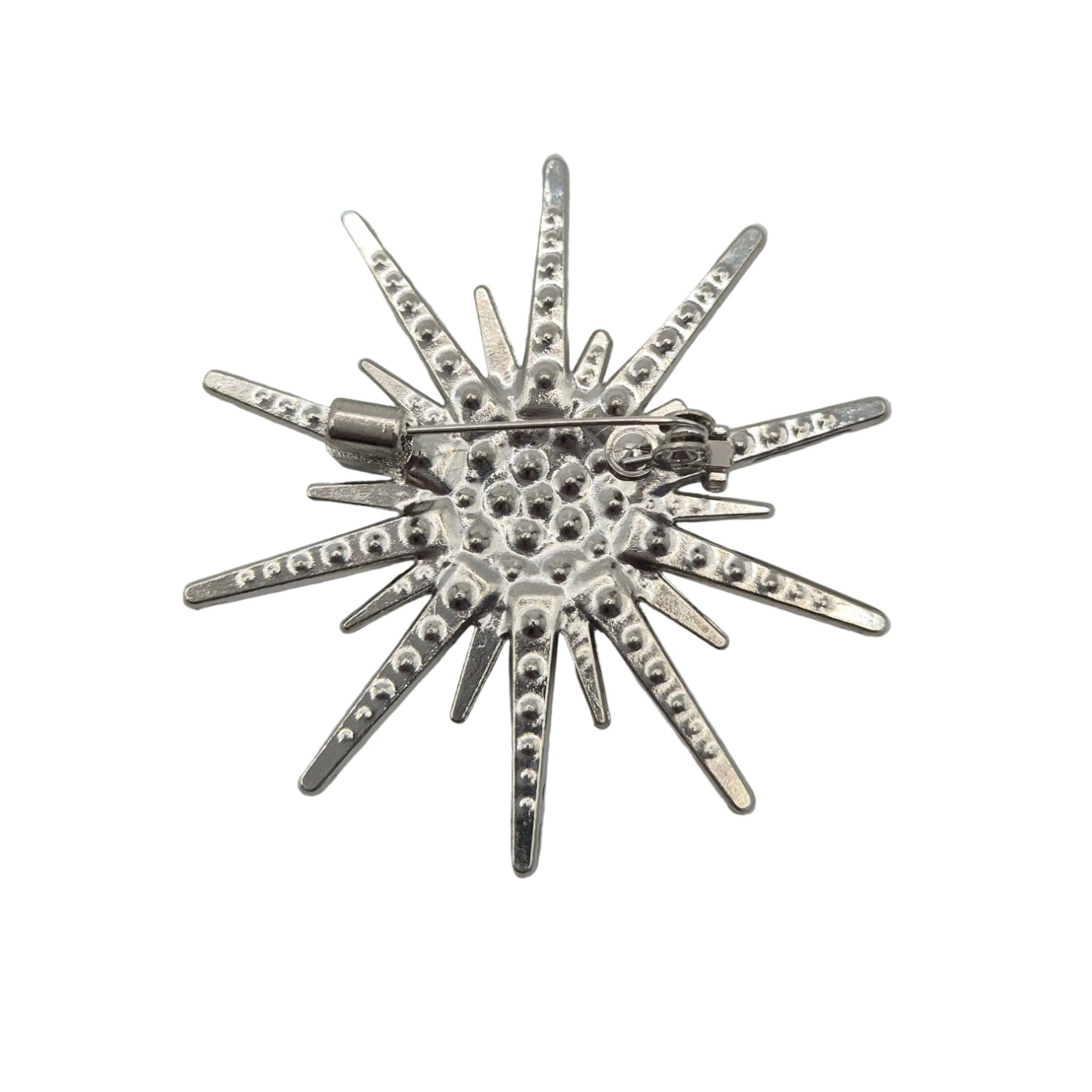 A silver starburst brooch with a textured center and pointed rays, photographed on a plain white background.