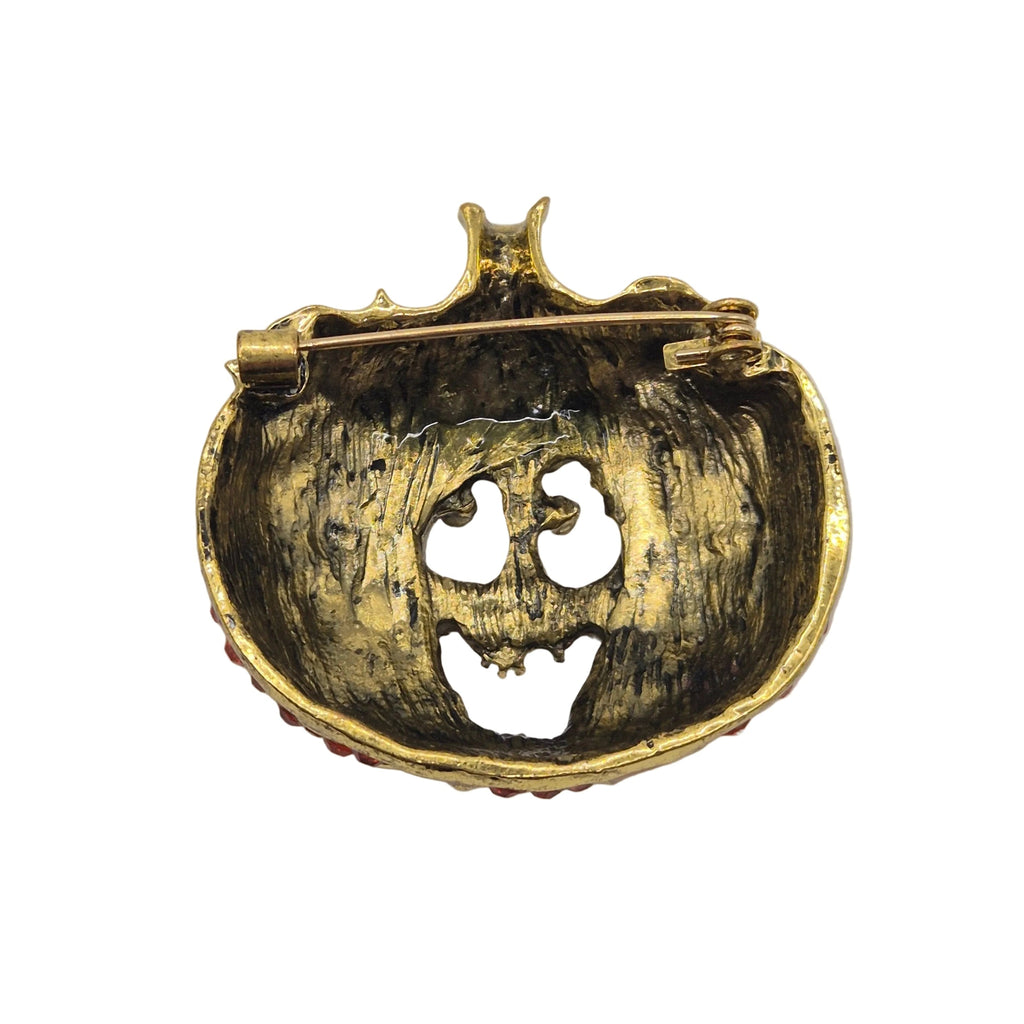 A vintage-style gold pumpkin-shaped brooch with a safety pin back, featuring a distressed gold finish and a carved jack-o'-lantern face.