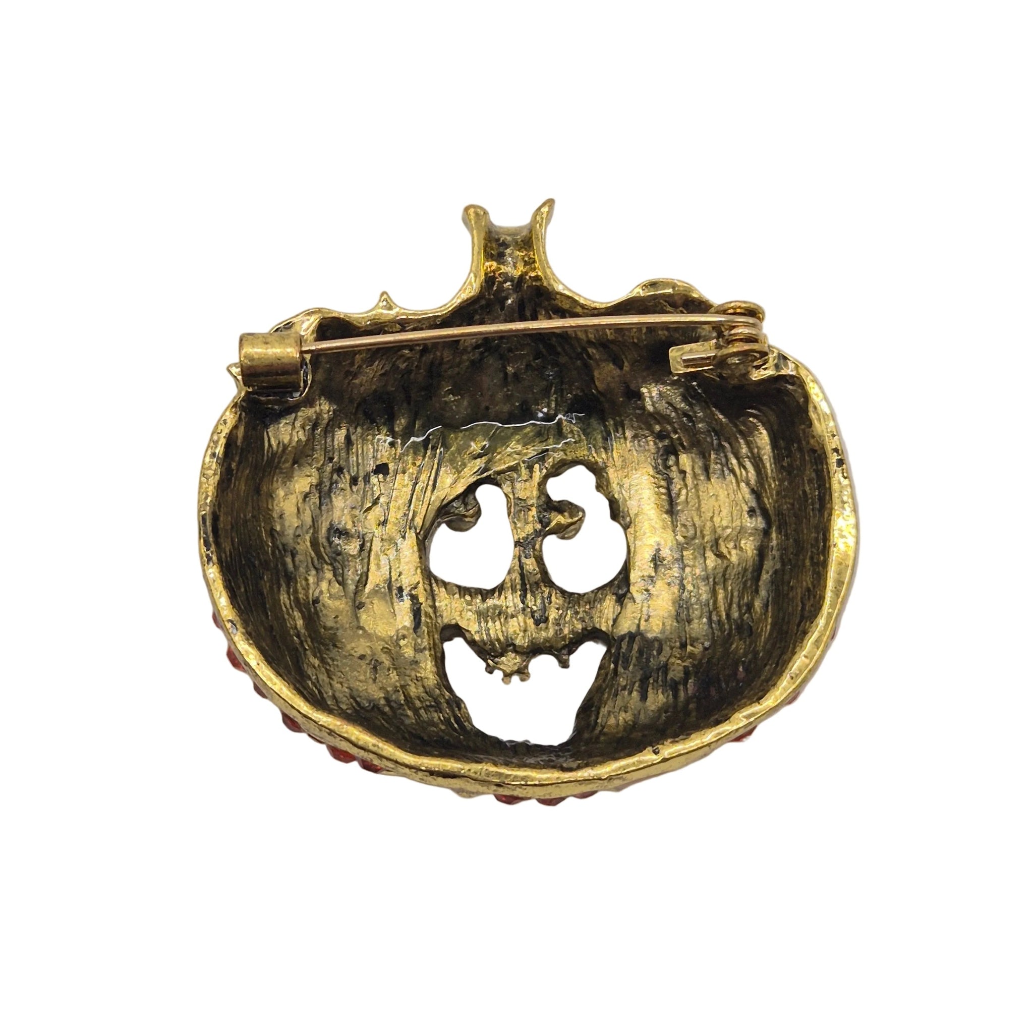 A vintage-style gold pumpkin-shaped brooch with a safety pin back, featuring a distressed gold finish and a carved jack-o'-lantern face.