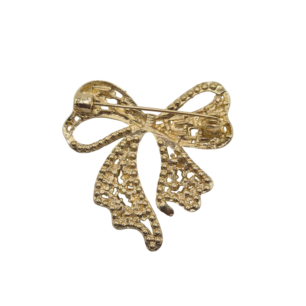 A gold bow-shaped brooch with a textured, beaded openwork design, photographed on a plain white background.