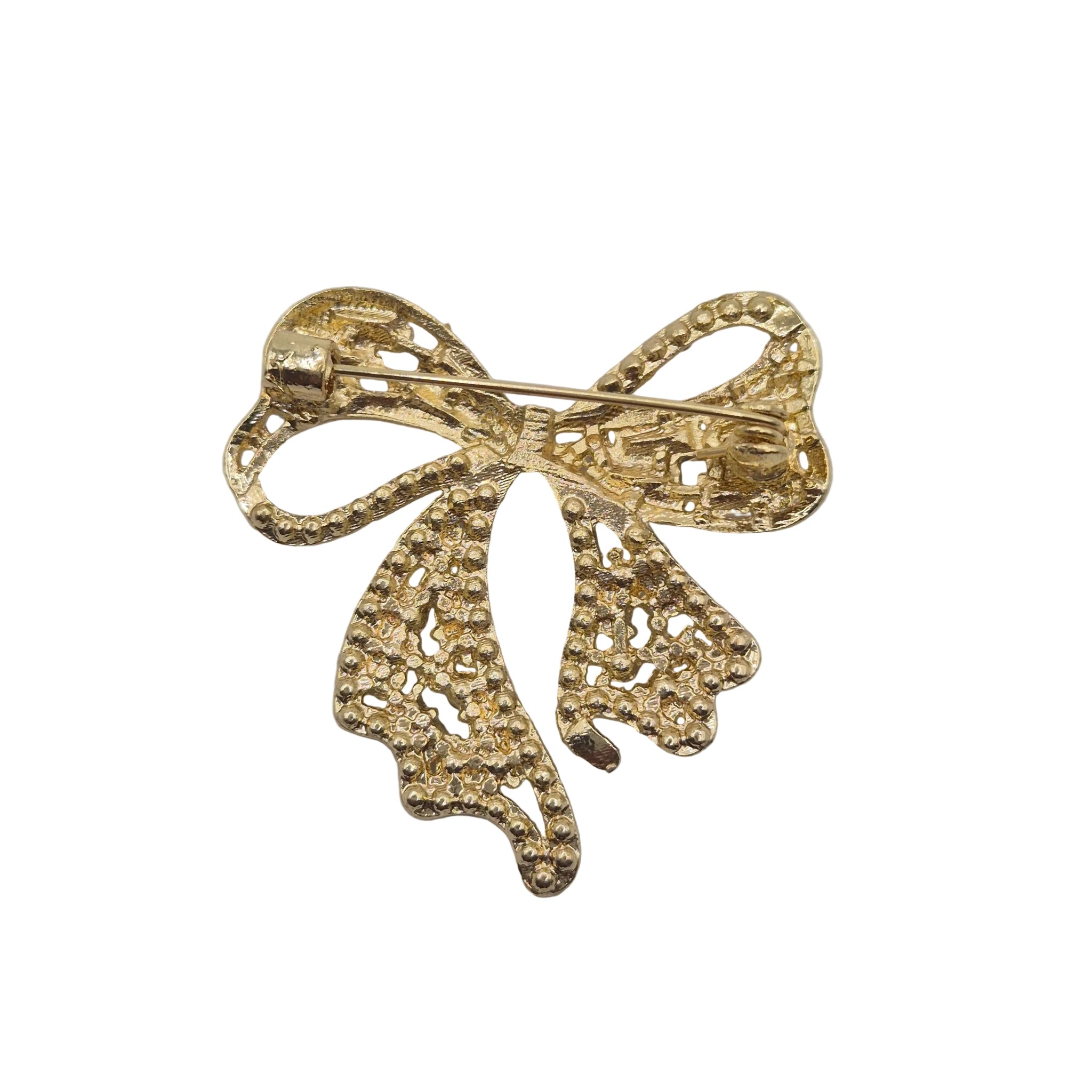 A gold bow-shaped brooch with a textured, beaded openwork design, photographed on a plain white background.
