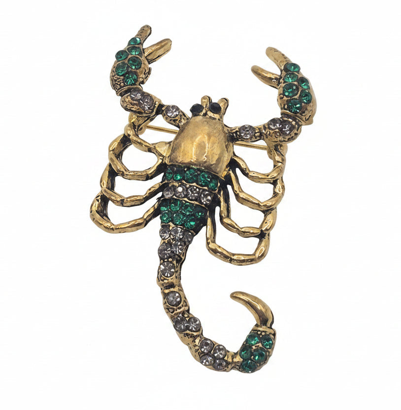 A gold-toned scorpion brooch embellished with green rhinestones, shown against a plain white background.