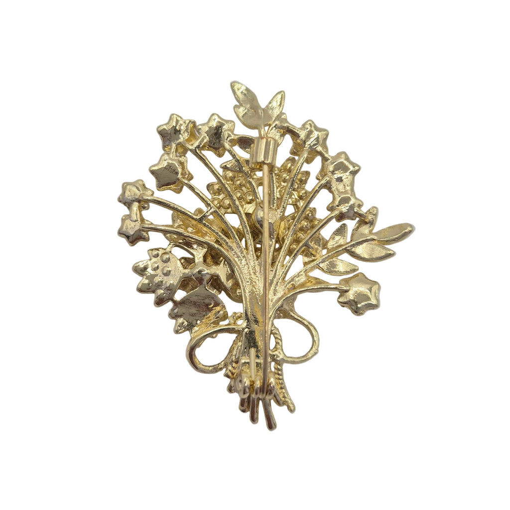 A vintage gold-tone floral brooch featuring stylized flowers and leaves, photographed on a plain light gray background.