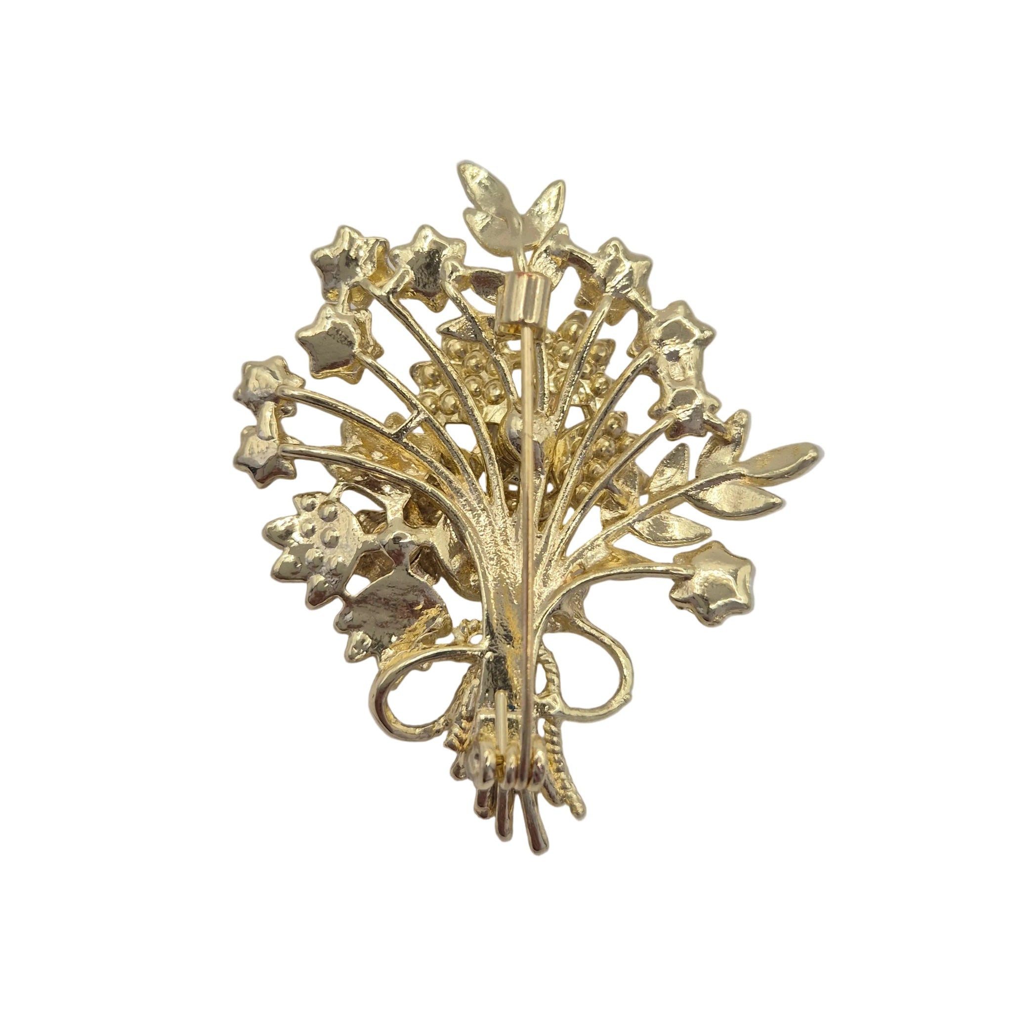 A vintage gold-tone floral brooch featuring stylized flowers and leaves, photographed on a plain light gray background.