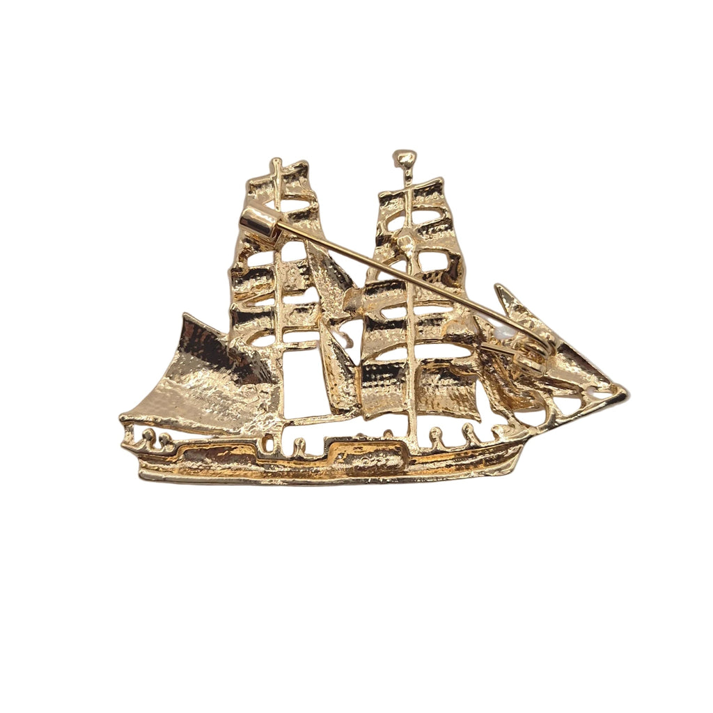 A gold-toned metal ship charm or brooch with multiple masts and sails, shown on a plain white background.