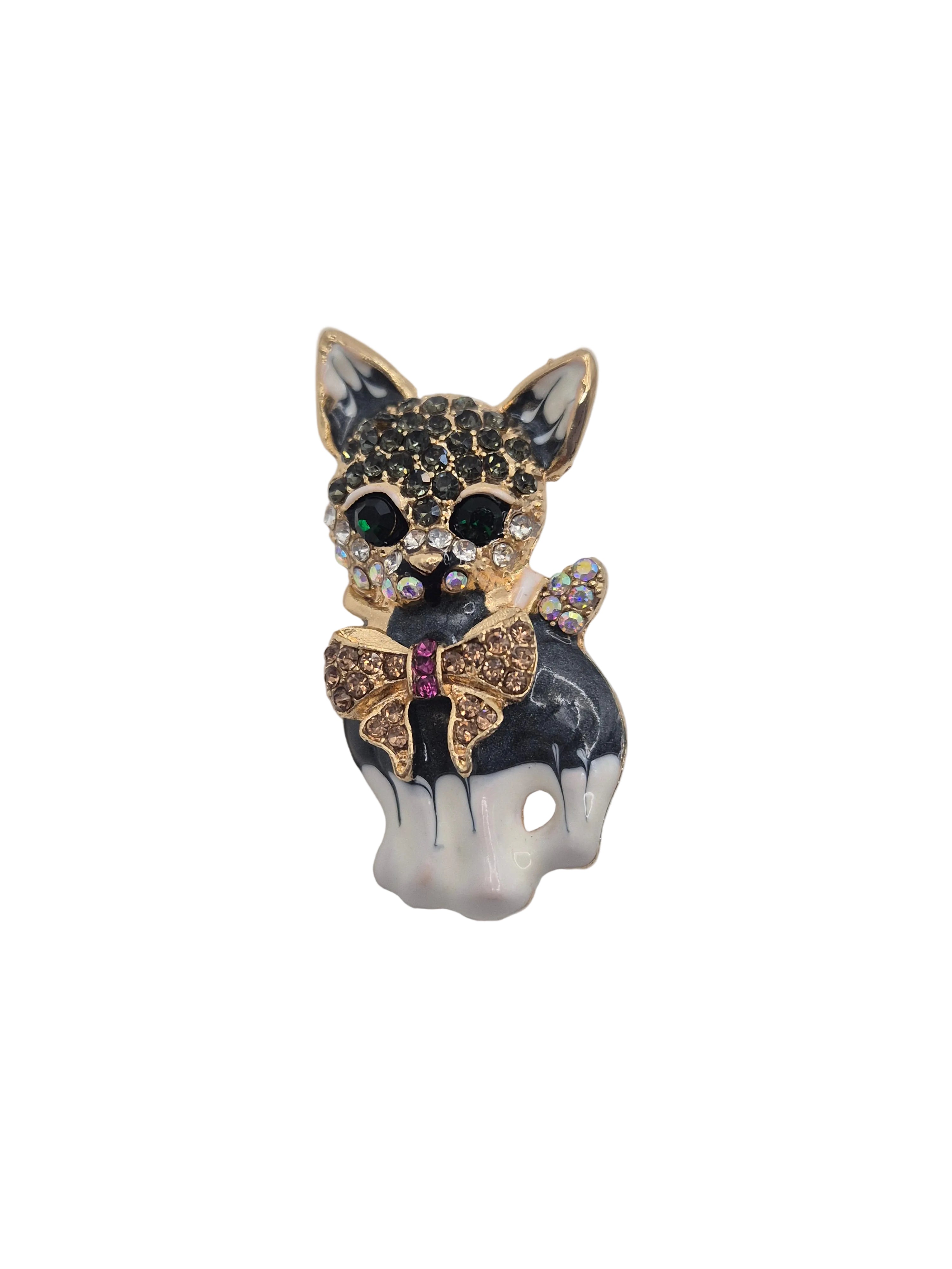 A small decorative cat-shaped brooch or charm with a black and white enamel body, gold-tone outlines, rhinestone detailing, and a bow motif on a plain white background.