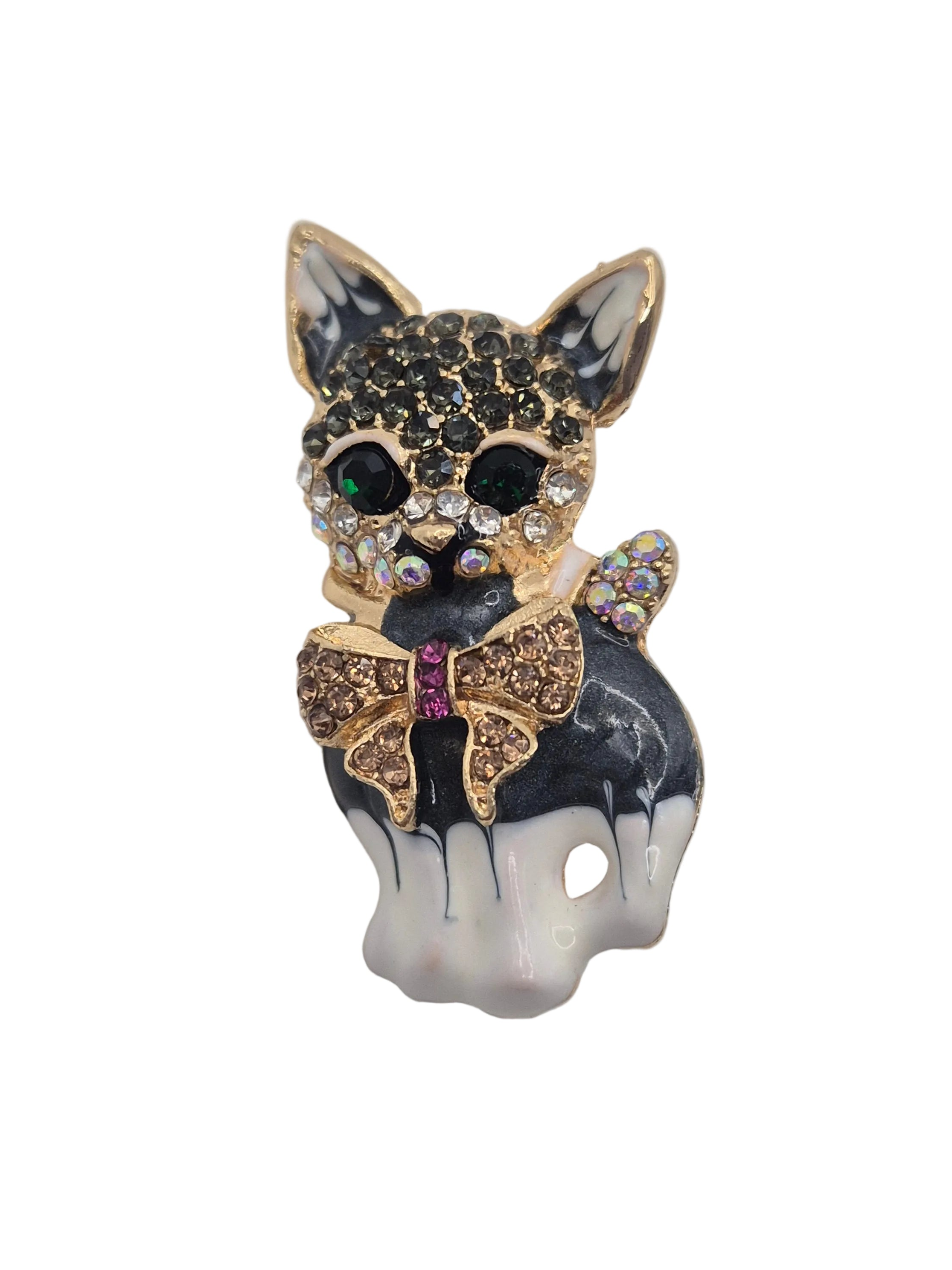 A small cat-shaped brooch or pin with a black and white dripping enamel finish, gold-tone outlines, rhinestone-covered ears and bow, and dark and iridescent eyes, shown on a plain white background.