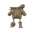 An antique gold tone metal pendant shaped like a knitted sweater with knitting needles and yarn balls, shown on a plain white background.