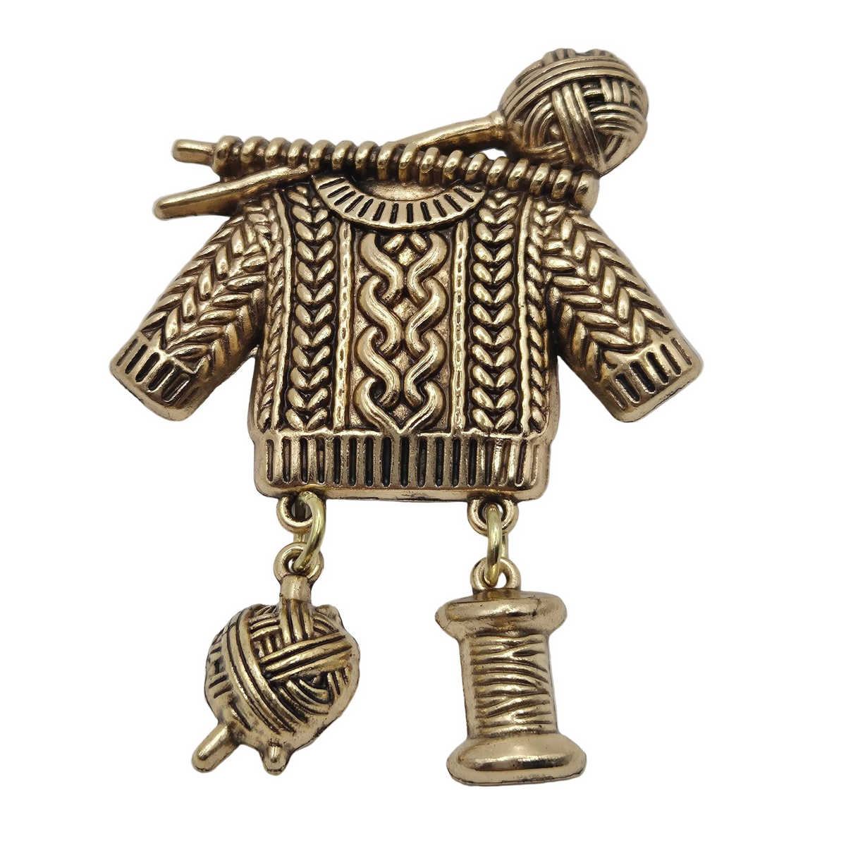 A vintage-style gold tone knitting-themed brooch shaped like a sweater with yarn balls and a spool of thread hanging from it, shown on a plain white background.