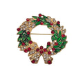 A gold-tone Christmas wreath brooch with green enamel leaves, red rhinestones, and a bow at the bottom decorated with clear rhinestones, shown on a plain light background.