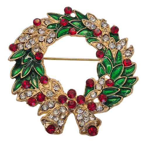 A gold-tone wreath brooch decorated with green enamel leaves, red faceted rhinestones, and a matching bow at the bottom, photographed on a plain white background.