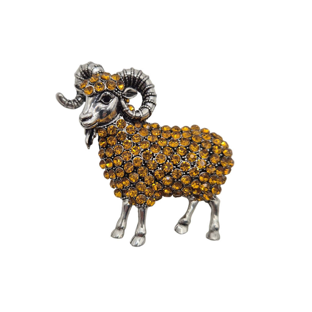 A ram-shaped brooch or pin featuring a silver-tone metal body and curved horns, covered with small round gold-tone rhinestones, shown on a plain white background.