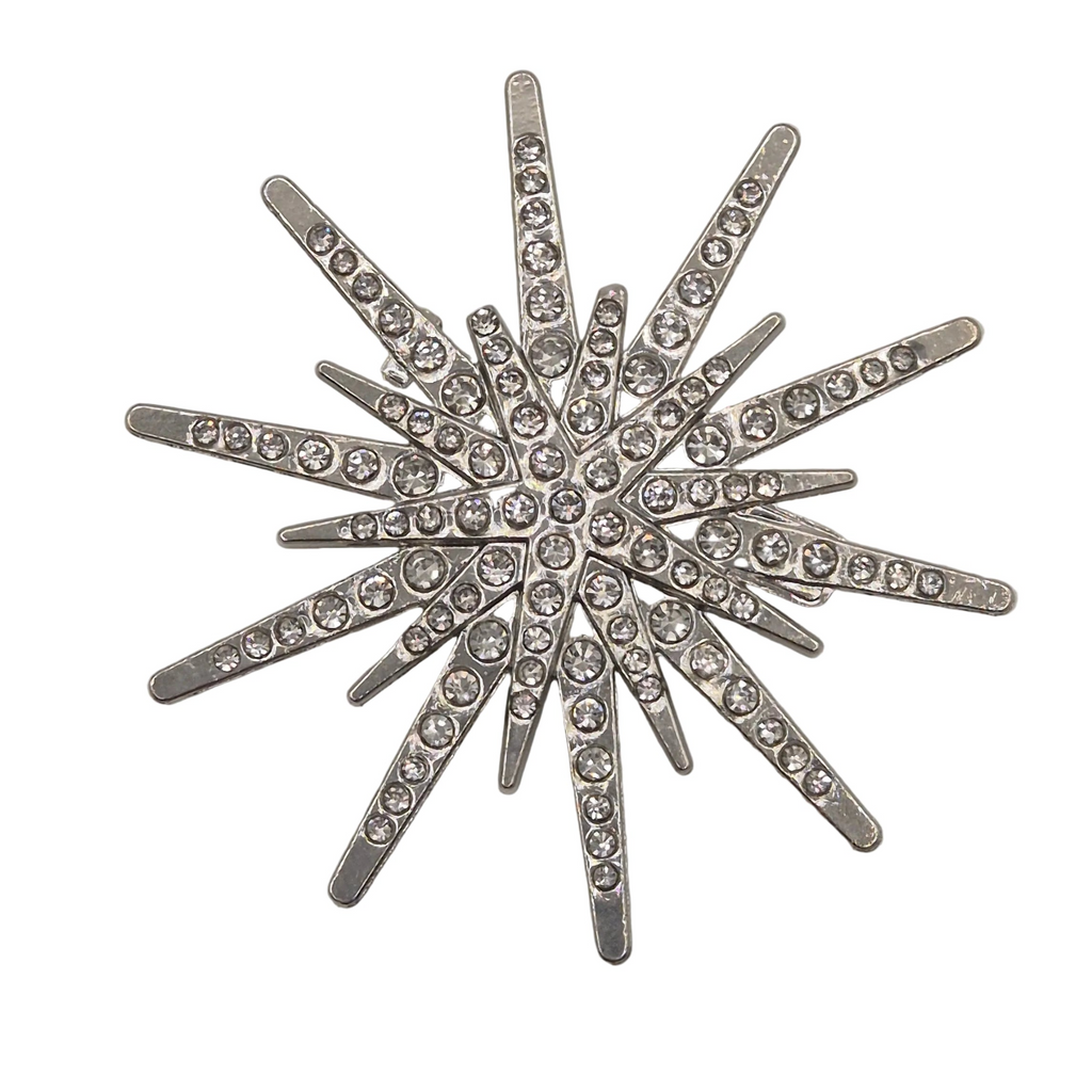 A silver-toned starburst brooch embellished with clear rhinestones, set against a plain white background.