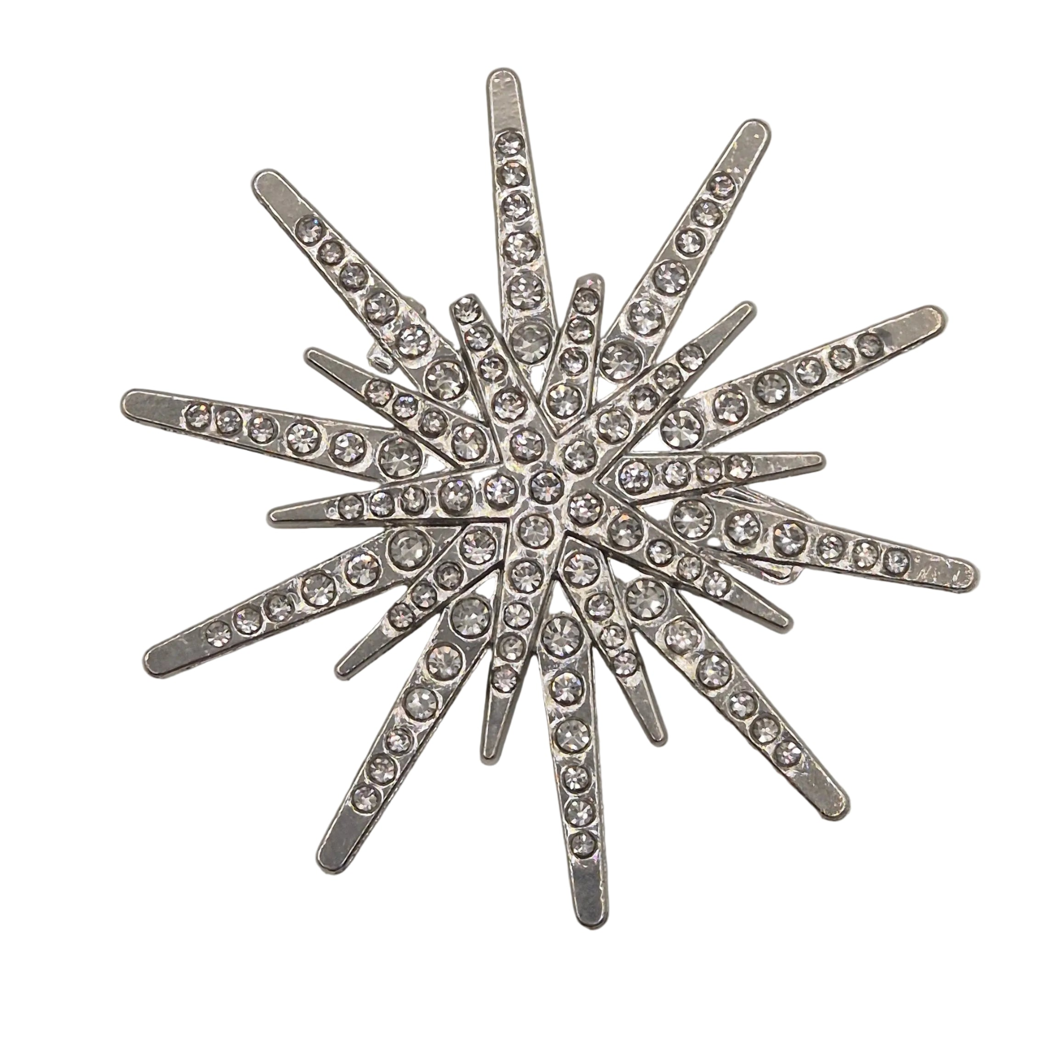 A silver-toned starburst brooch embellished with clear rhinestones, set against a plain white background.