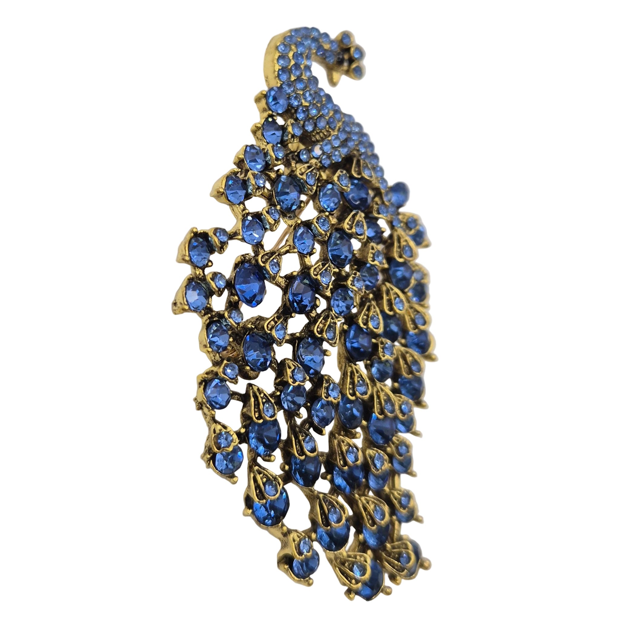 A peacock-shaped brooch featuring blue rhinestones set in gold-tone metal, photographed on a plain white background.