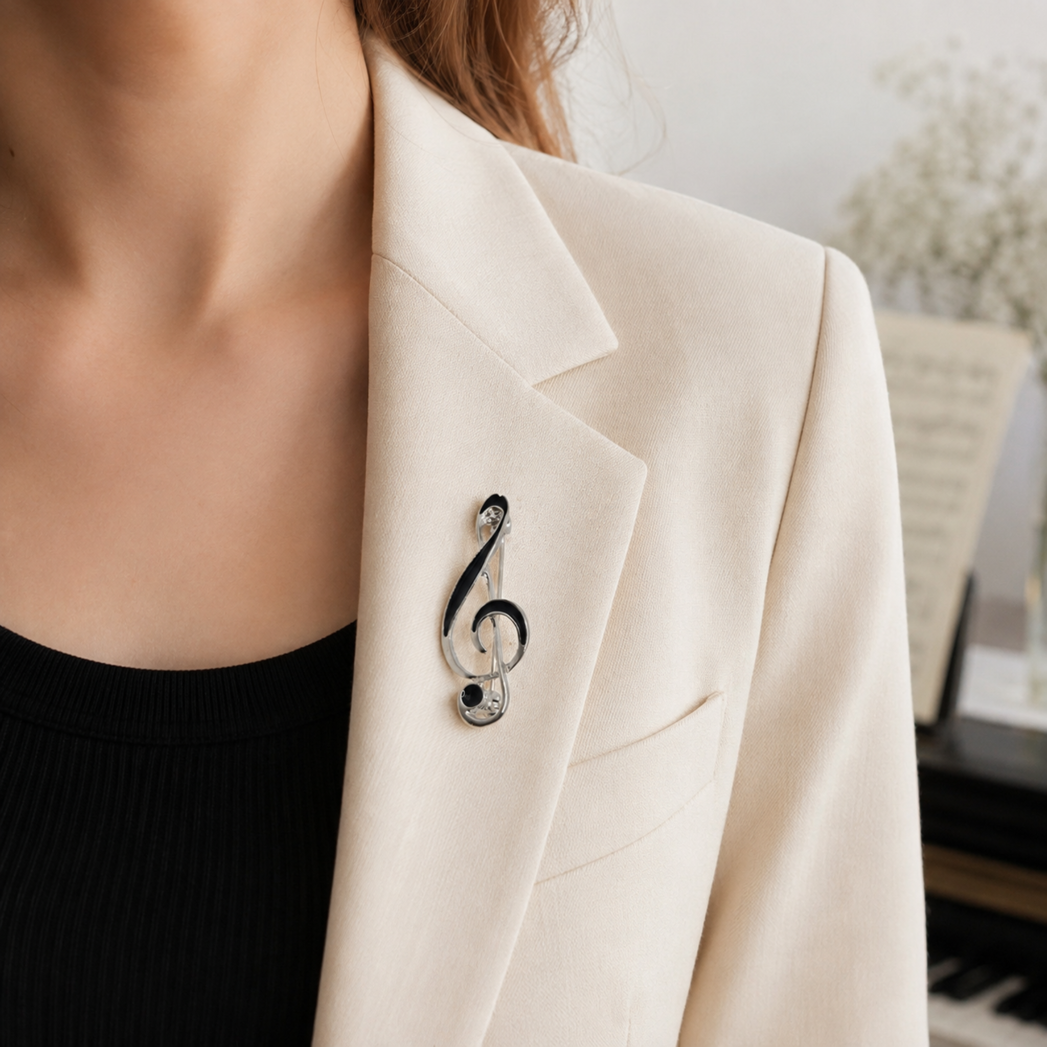 A close-up of a woman wearing a black and silver treble clef brooch pinned to the lapel of a cream-colored blazer.